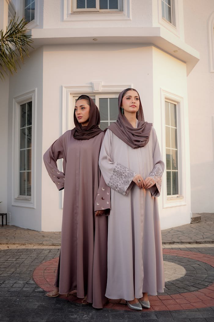 Two women in stylish abayas pose elegantly outdoors, showcasing modest fashion.