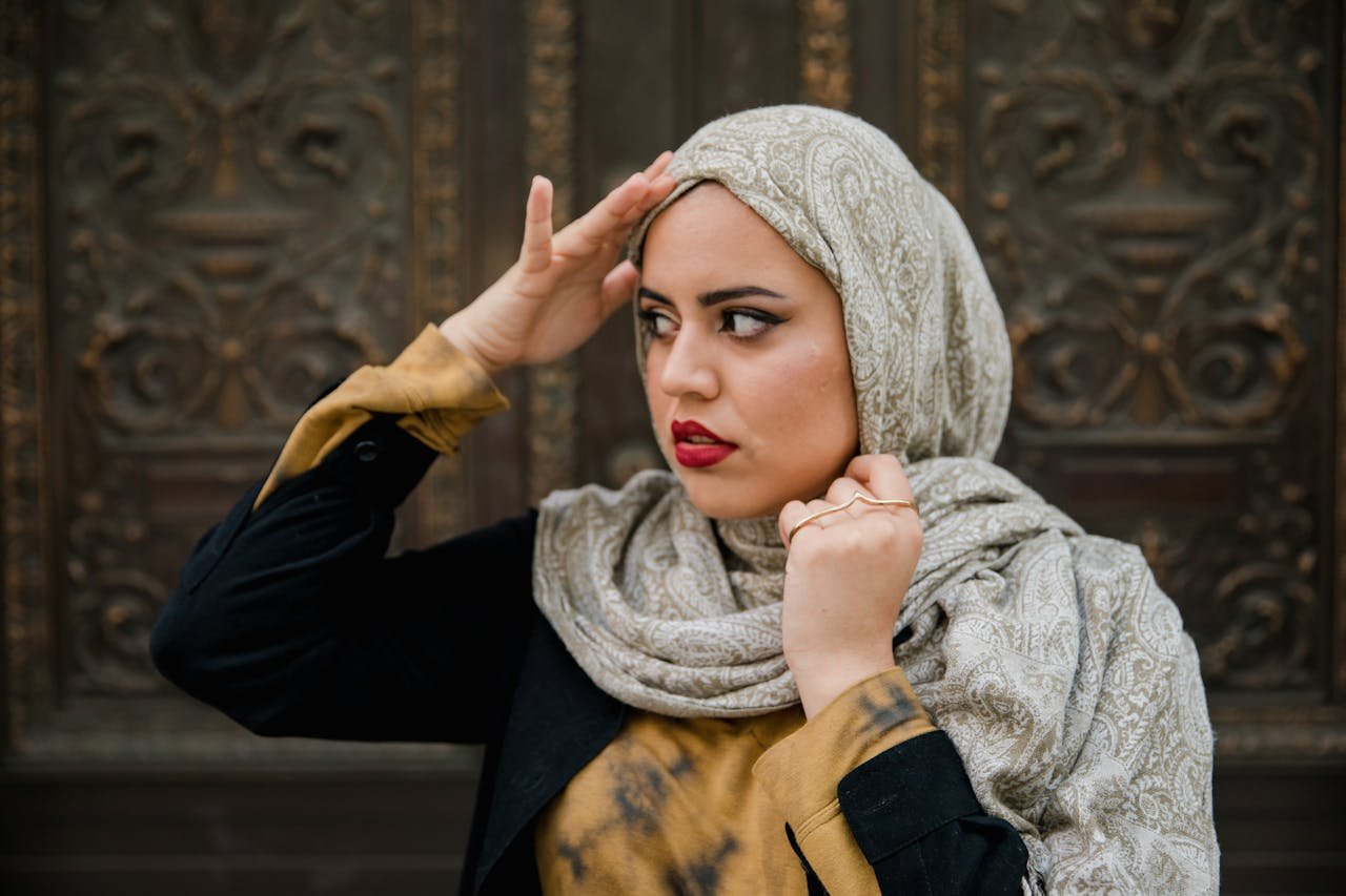 Elegant woman in a patterned hijab, posing outdoors against a textured background.
